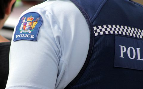 The image shows a police officer's uniform with a blue shoulder patch labeled "POLICE" and a checkerboard pattern, symbolizing authority and law enforcement presence.