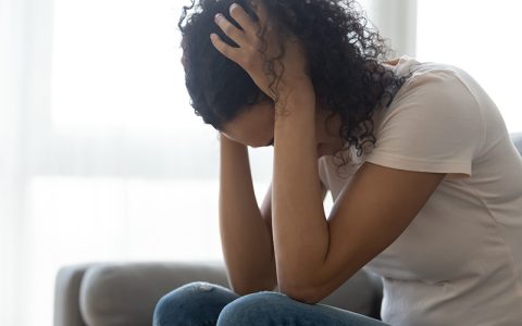 Female sitting on a couch inside a house, head in hands, in despair - victim of rape, sexual assault or domestic violence
