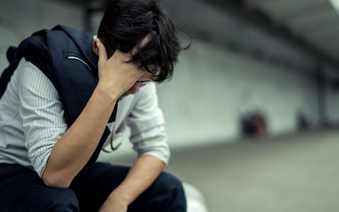 Stressed man (detective) sitting on a bench with head in hands
