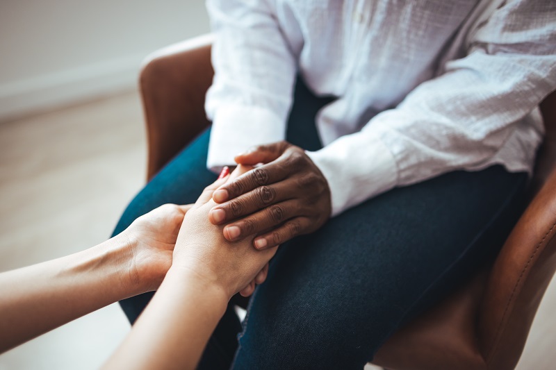 Biracial female psychologist hands holding palms of millennial woman patient