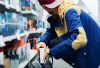 A person in a brightly colored jacket is crouching in a store aisle, discreetly placing an item into a backpack, suggesting a potential shoplifting incident.