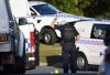 A Queensland Police officer secures a crime scene with tape, surrounded by police vehicles. Evidence markers indicate an investigation is underway, emphasizing the role of law enforcement in ensuring public safety.