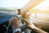 Drivers hands on steering wheel, with hands free phone attached to windscreen