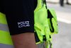 The image features a police officer's arm wearing a black shirt embroidered with "POLICE SCOTLAND," alongside a bright yellow high-visibility vest, conveying authority and safety in law enforcement.