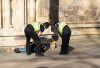 Two uniform police officers checking on the welfare of a man laying on the pavement