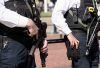 Two police officers stand ready, one holding an assault rifle and another equipped with various tools. Their presence suggests security and law enforcement in an active environment.