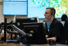 Motorola feature image. A focused operator sits at a desk with multiple monitors, managing data and communications in a busy command center, essential for coordinating police operations and public safety responses.