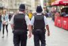 The image shows two police officers walking away, wearing uniforms and hats, amidst a bustling city street filled with people. Their presence suggests a focus on public safety.