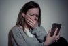 Sad desperate young teenager female girl on smart phone suffering from online bullying, sextortion, harassment felling lonely and hopeless sitting on bed at night.
