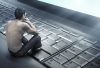 Conceptual photo of a young man sitting on a large laptop keyboard staring at the screen, addicted to the internet, dangers of online extremism misogyny radicalisation