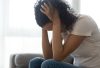 Female sitting on a couch inside a house, head in hands, in despair - victim of rape, sexual assault or domestic violence