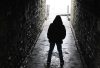 A solitary young person stands in a dark tunnel, backlit by bright light at the exit, evoking themes of isolation and transition, relevant to discussions on community safety and policing.